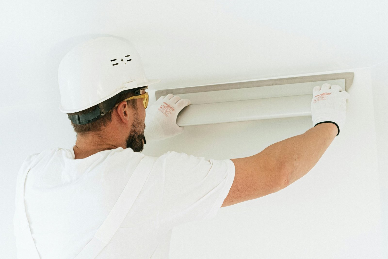 A construction worker wearing safety gear installs a light fixture in a modern indoor setting.